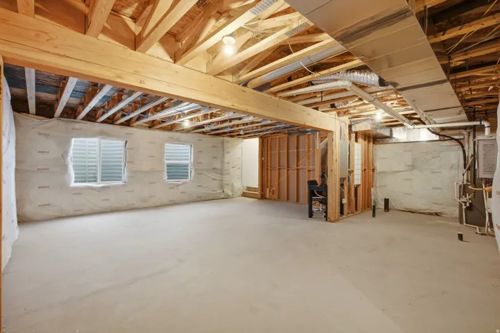 Unfinished basement featuring exposed wood joists and framing, concrete flooring, two egress windows with horizontal blinds, and visible ductwork