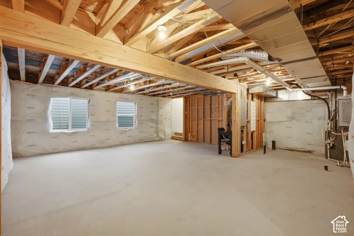 Unfinished basement featuring exposed wood joists and framing, concrete flooring, two egress windows with horizontal blinds, and visible ductwork