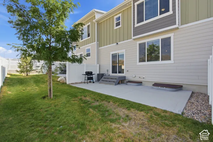 Rear exterior featuring a concrete patio, sliding glass door access, and a fenced yard with mature trees