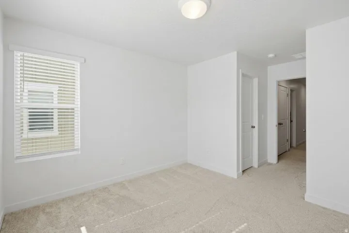 Neutral tone carpeting, white walls, flush mount ceiling light fixture, white window blinds, and white interior doors with round knob hardware