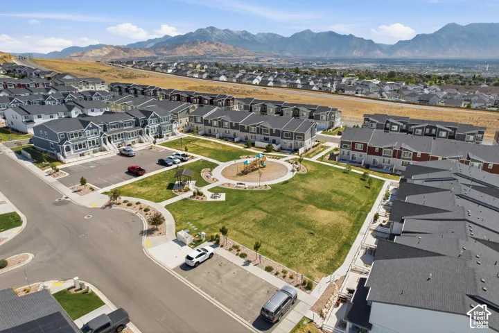 Expansive green space featuring a playground, walking paths, and mature landscaping, surrounded by multi-story residential properties with mountain scenery