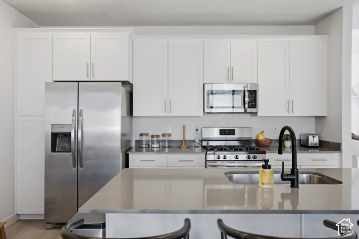 Kitchen featuring white shaker-style cabinetry, stainless steel appliances, a gas range, and a kitchen island with an undermount sink and matte black faucet
