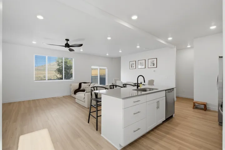Open-concept living space featuring a central kitchen island with a single-basin sink and stainless steel faucet, wood-finish flooring, recessed lighting, and large windows