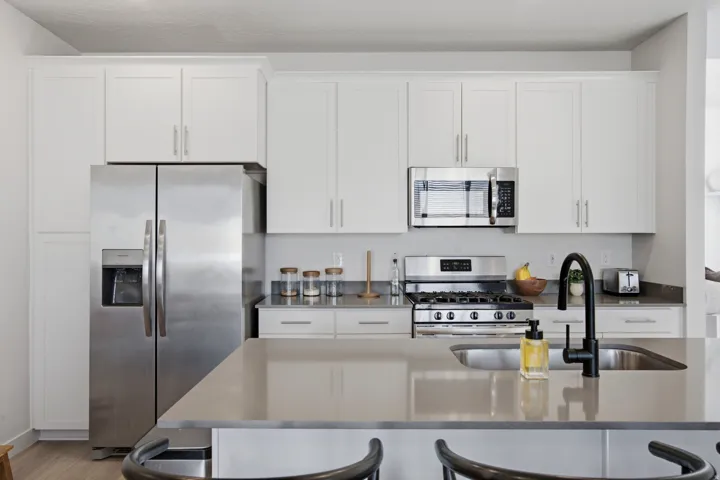 Kitchen featuring white shaker-style cabinetry, stainless steel appliances, a gas range, and a kitchen island with an undermount sink and matte black faucet