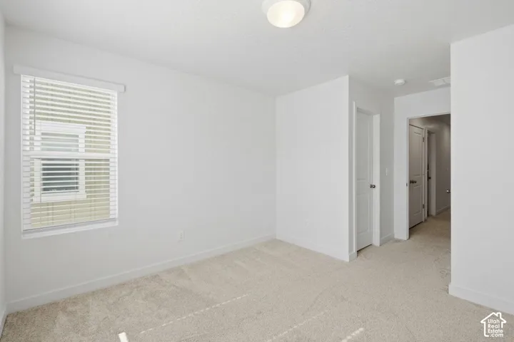 Neutral tone carpeting, white walls, flush mount ceiling light fixture, white window blinds, and white interior doors with round knob hardware