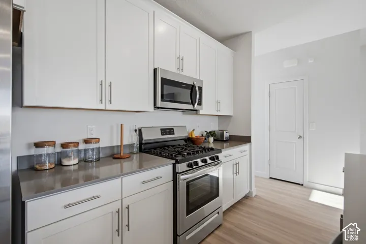 Modern kitchen featuring white shaker cabinetry with brushed nickel hardware, stainless steel appliances, grey countertops, and light wood-finish flooring