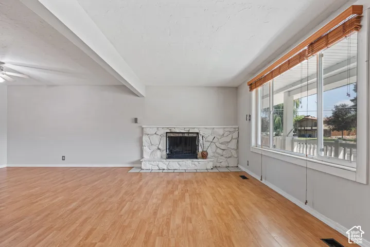 Spacious room featuring wood-finish flooring, a white stone fireplace, and a large multi-pane window with wooden blinds