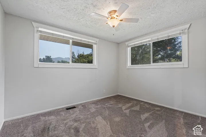 Room featuring two windows with white blinds, gray textured carpeting, and a ceiling fan with integrated lighting