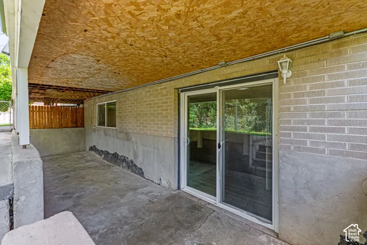 Exterior patio with concrete flooring, supported by white columns and a wood-paneled ceiling