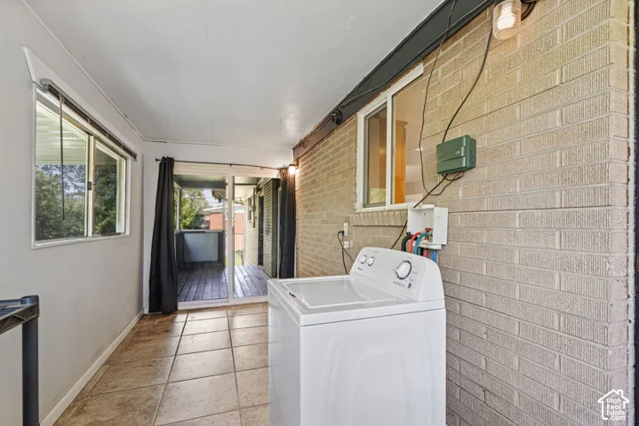 Enclosed laundry area featuring tile flooring, a brick accent wall, and direct access to an outdoor deck through sliding glass doors