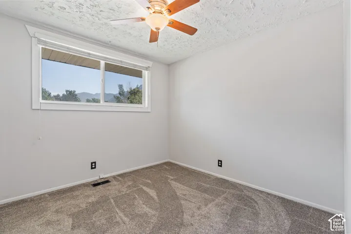 Carpeted room with a ceiling fan, white walls, and a window with mountain scenery