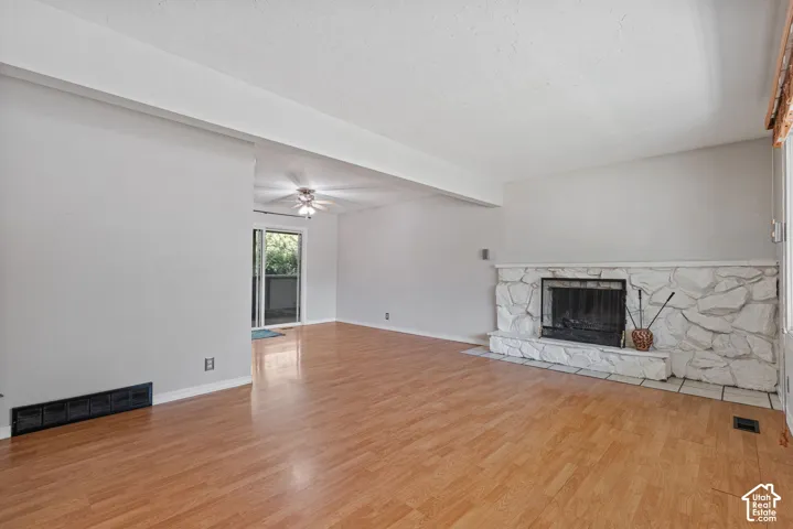 Spacious living area featuring wood-finish flooring, a stone-clad fireplace with hearth, and light-toned walls