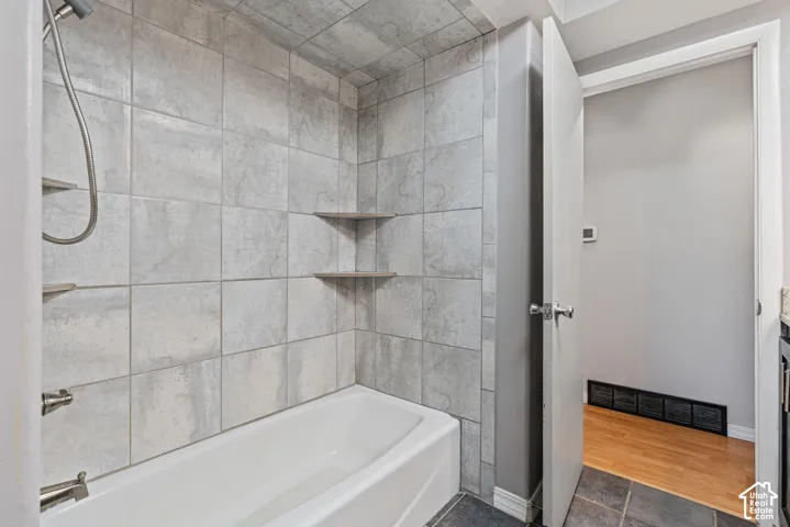Bathtub and shower combination featuring grey-toned tile surround with two built-in corner shelves
