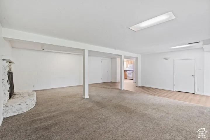 Expansive finished room featuring a stone fireplace, carpeted flooring, and a portion with wood-finish flooring