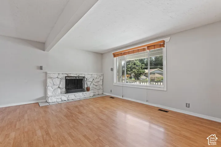 Living space featuring wood-finish flooring, a stone-clad fireplace with a hearth, and a large window with blinds