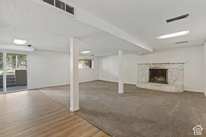Spacious room featuring a stone fireplace, wood-finish flooring, and carpeted areas