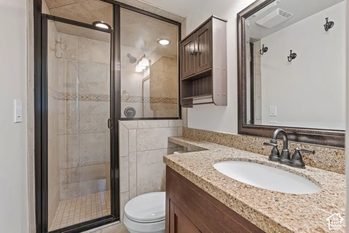 Bathroom featuring a glass-enclosed shower with tile surround, a built-in vanity with a granite-finish countertop, an undermount sink, and a framed wall mirror