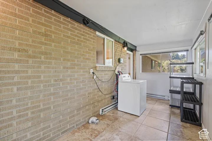 Enclosed utility area featuring light-toned brick wall, multiple window exposures, a tiled floor, and a built-in wall-mounted light fixture