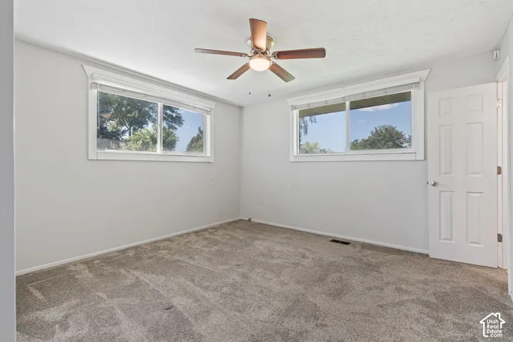 Spacious room featuring neutral carpeting, light-toned walls, and a ceiling fan with integrated lighting