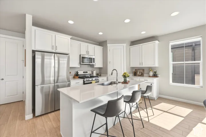 Kitchen featuring a large central island with seating, white shaker cabinetry, stainless steel appliances, and light wood-finish flooring