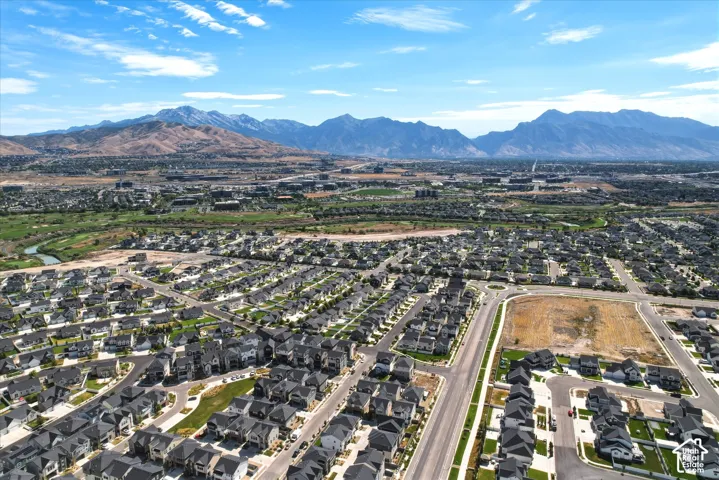 Expansive aerial view showcasing a developed residential neighborhood with structured streets, a nearby green space with a winding river, and a distant mountain range backdrop