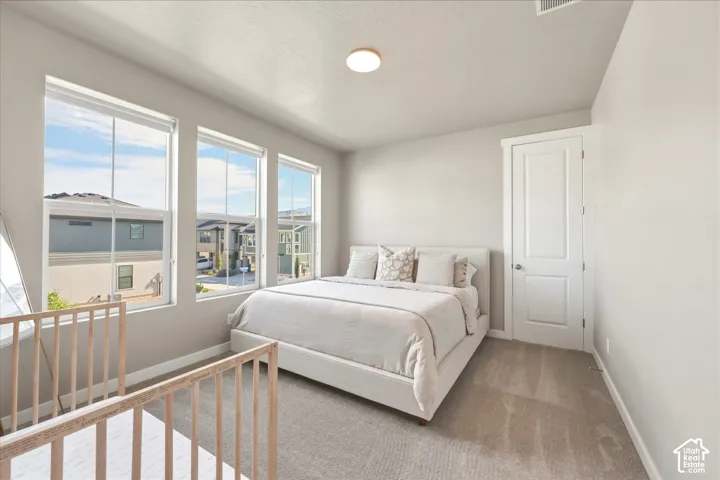 Spacious bedroom featuring light neutral wall tones, three large windows, a single panel door, and light-toned carpet flooring