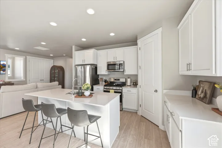 Kitchen featuring an island with sink, stainless steel appliances, white cabinetry, recessed lighting, and wood-finish flooring
