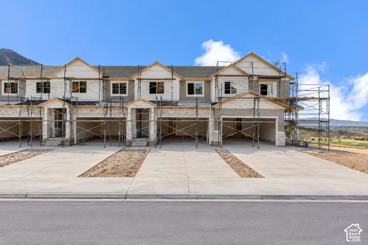 Multi-unit residential exterior featuring a multi-gabled roofline, stone veneer accents, integrated garage bays, and concrete driveways