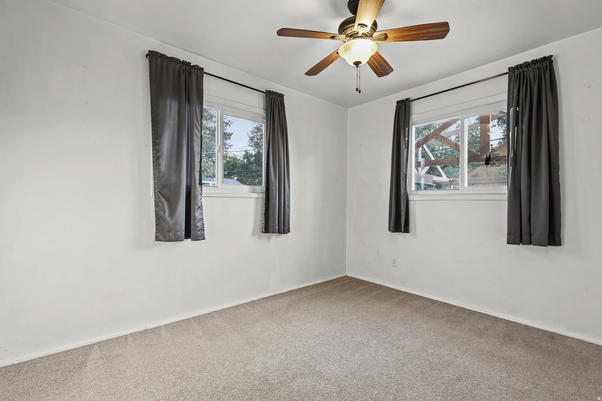 Neutral-toned carpet flooring, two windows with white trim, and a ceiling fan with integrated lighting