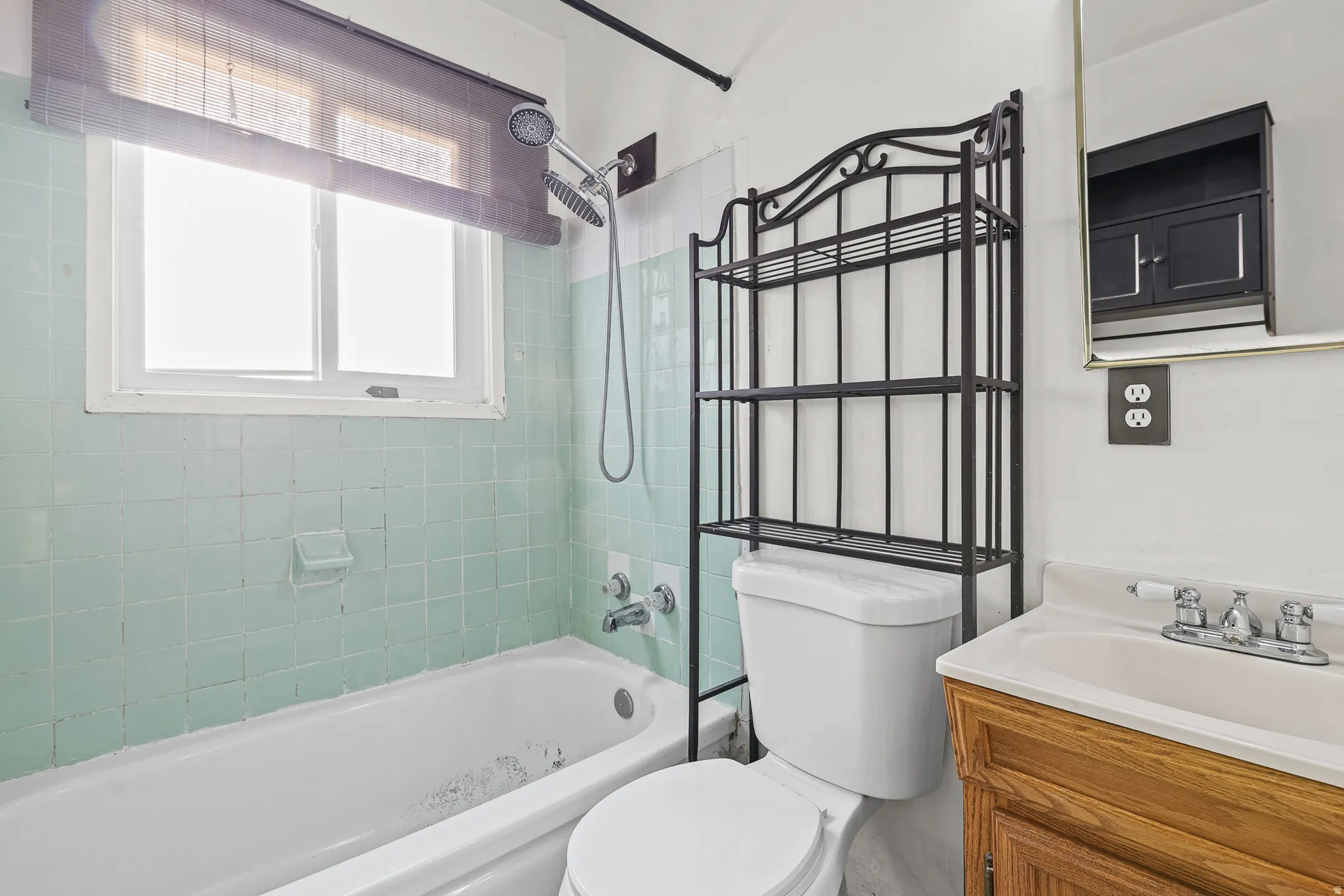 White bathtub with subway tile surround, single window, and a wood-finish vanity with an integrated sink