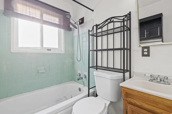 White bathtub with subway tile surround, single window, and a wood-finish vanity with an integrated sink