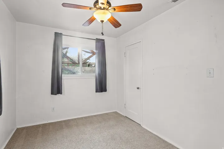 Recessed window with exterior framework, ceiling fan with light fixture, light-toned carpet, white painted walls, and a white door with a silver-toned knob