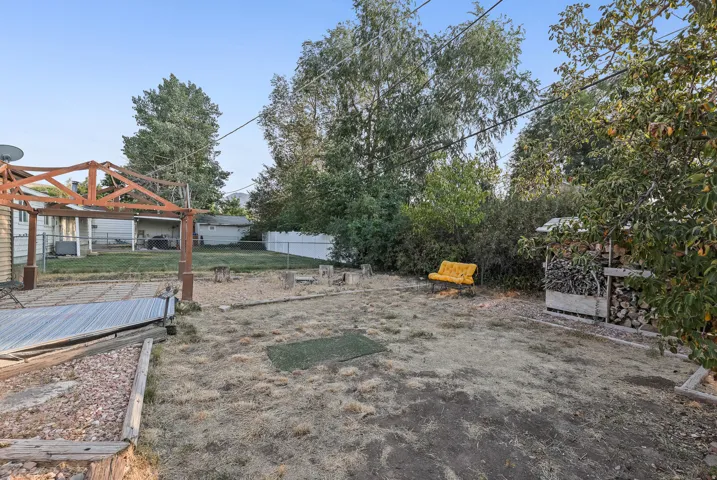 Backyard featuring a wooden pergola, wood-framed raised garden bed, and a stacked wood storage structure