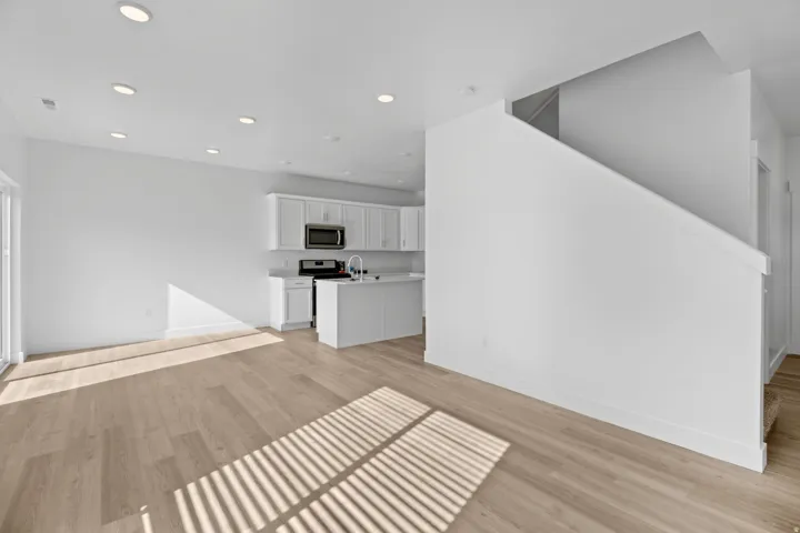 Open-concept living area featuring wood-finish flooring, recessed lighting, and a white kitchen with a built-in microwave and stainless steel appliances