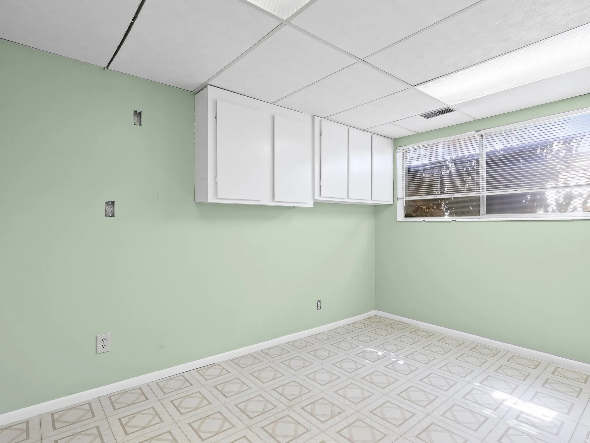 Room featuring patterned tile flooring, light green walls, and a drop ceiling with integrated lighting