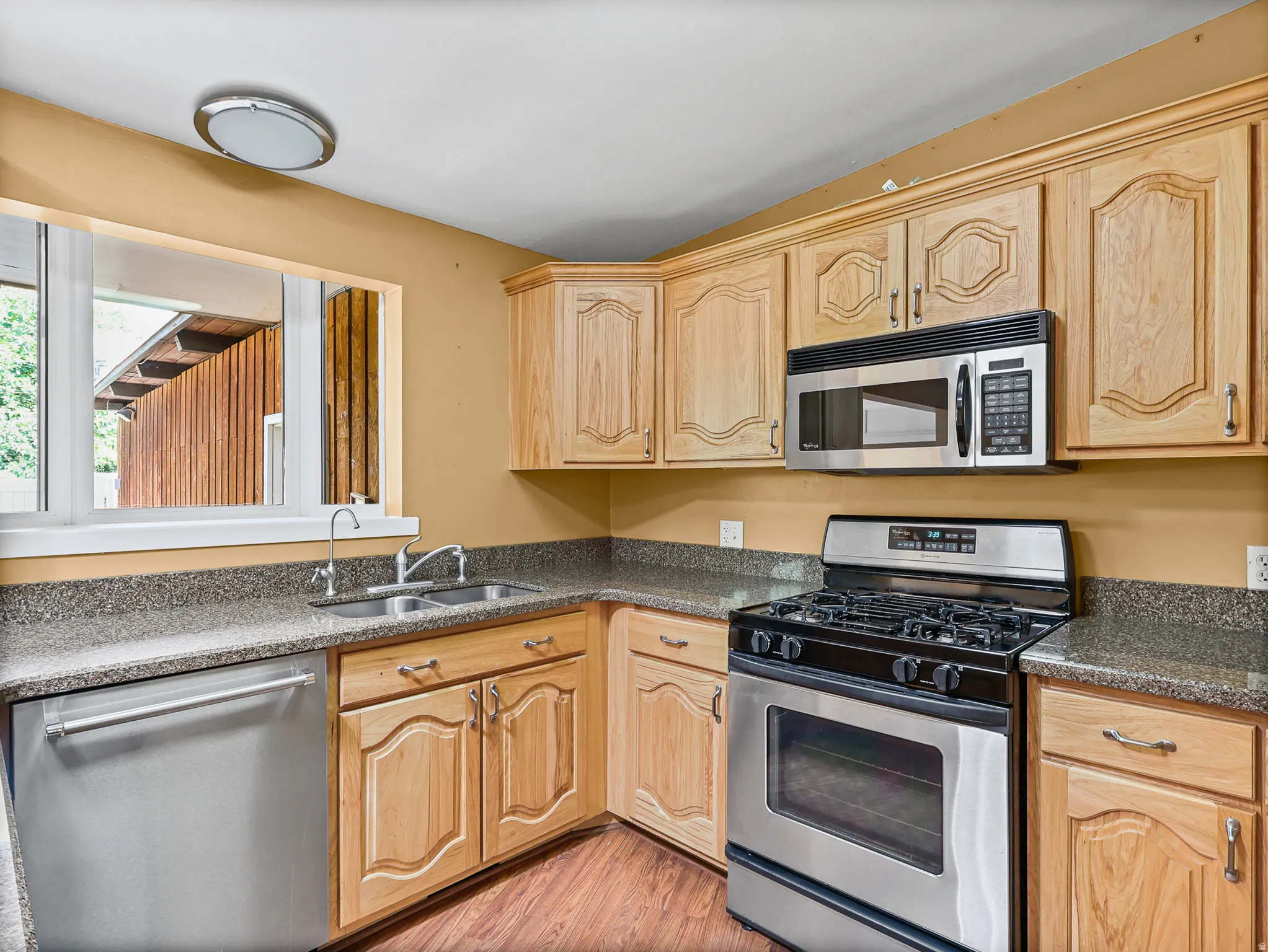 Kitchen featuring light wood cabinetry, stone-look countertops, and wood-finish flooring