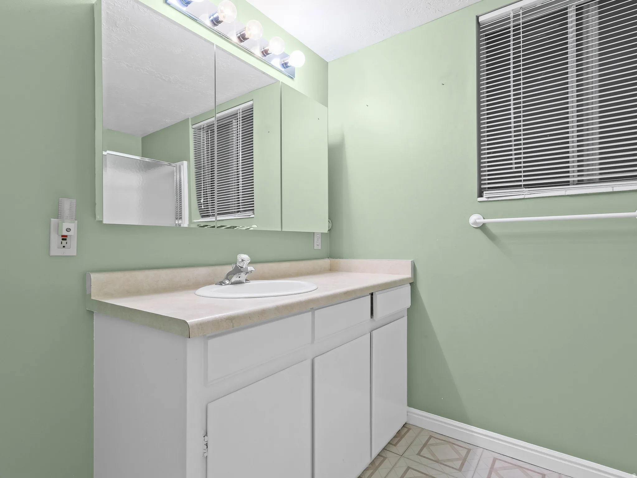 Bathroom featuring a single vanity with an integrated sink, a large wall mirror, and overhead strip lighting