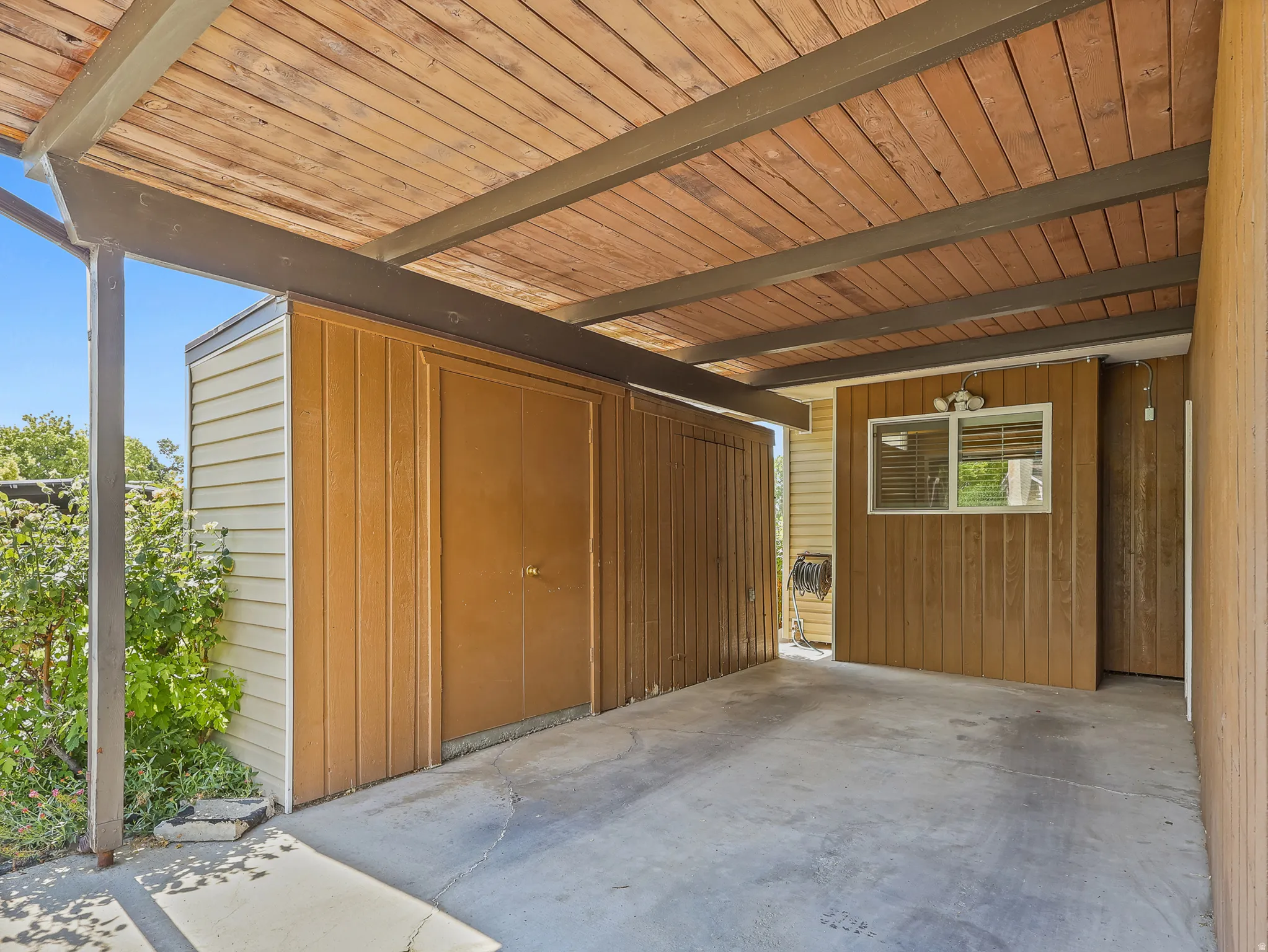 Covered carport with a wood-finish ceiling, exposed metal beams, and a concrete slab