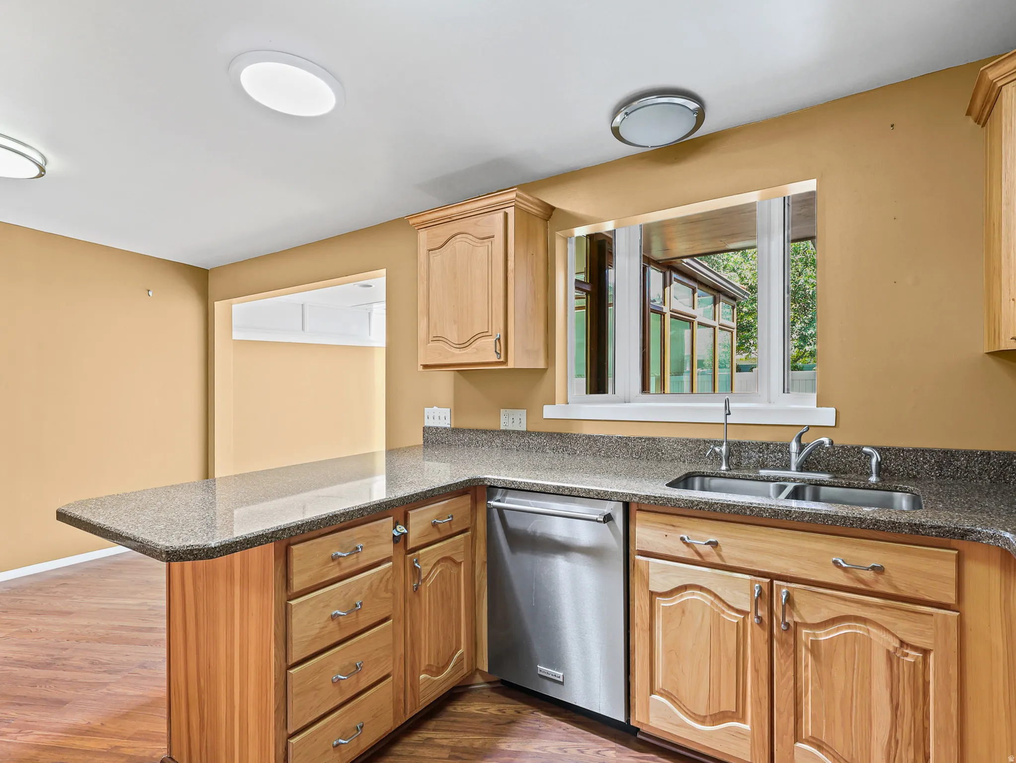 Kitchen featuring wood cabinetry, a stainless steel dishwasher, a double-basin sink, and speckled countertops