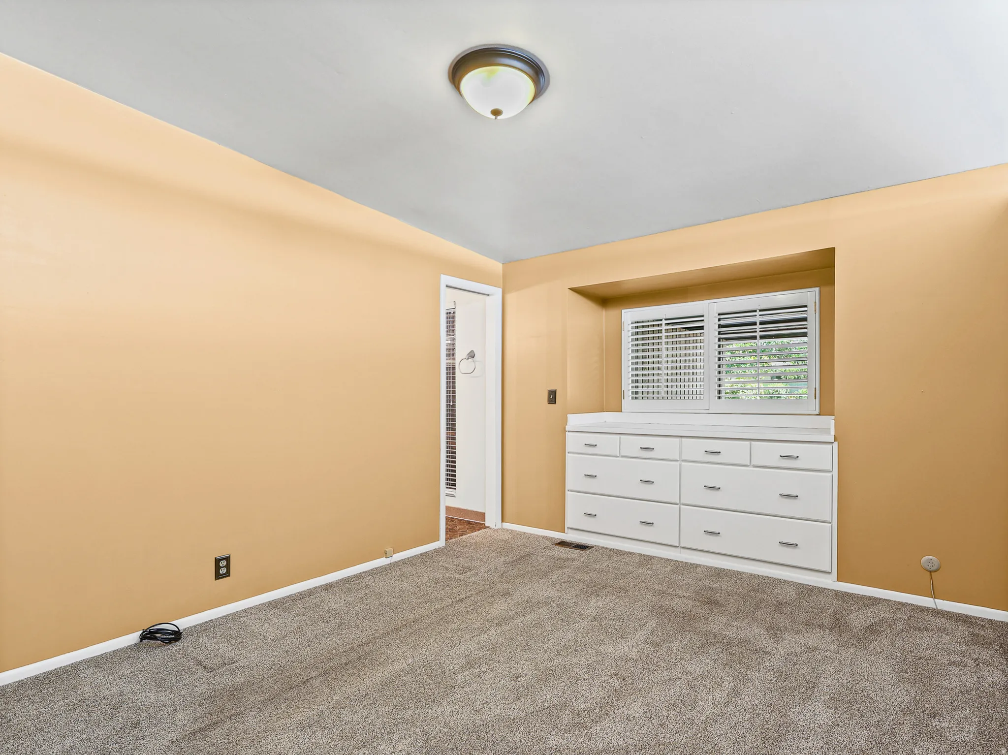 Carpeted interior space featuring a built-in window seat with integrated drawers and a window with white shutters