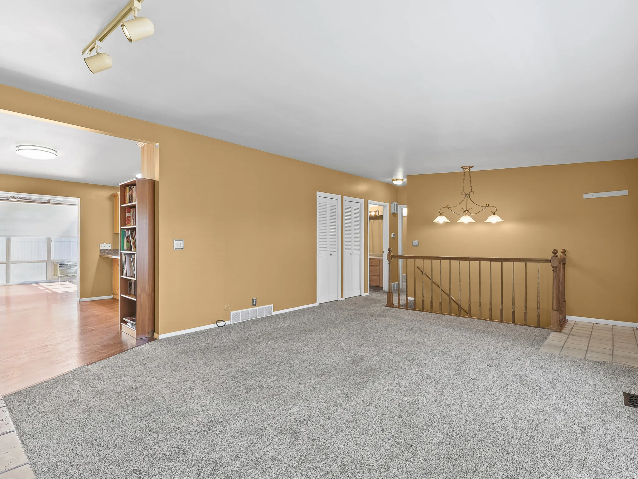 Carpeted living area featuring track lighting, a decorative chandelier, white bi-fold closet doors, and wood banister
