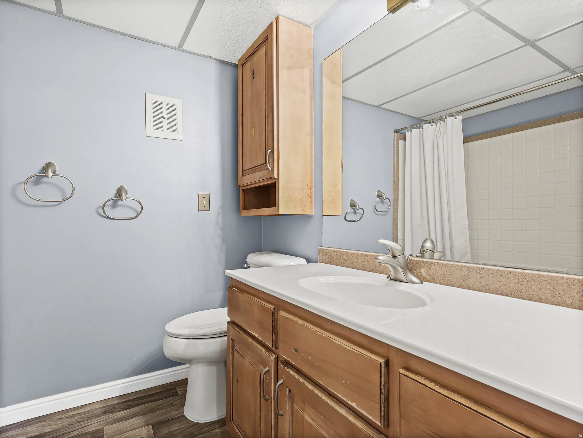 Bathroom featuring a single vanity with an integrated sink, wood-finish cabinetry, and a large wall-mounted mirror