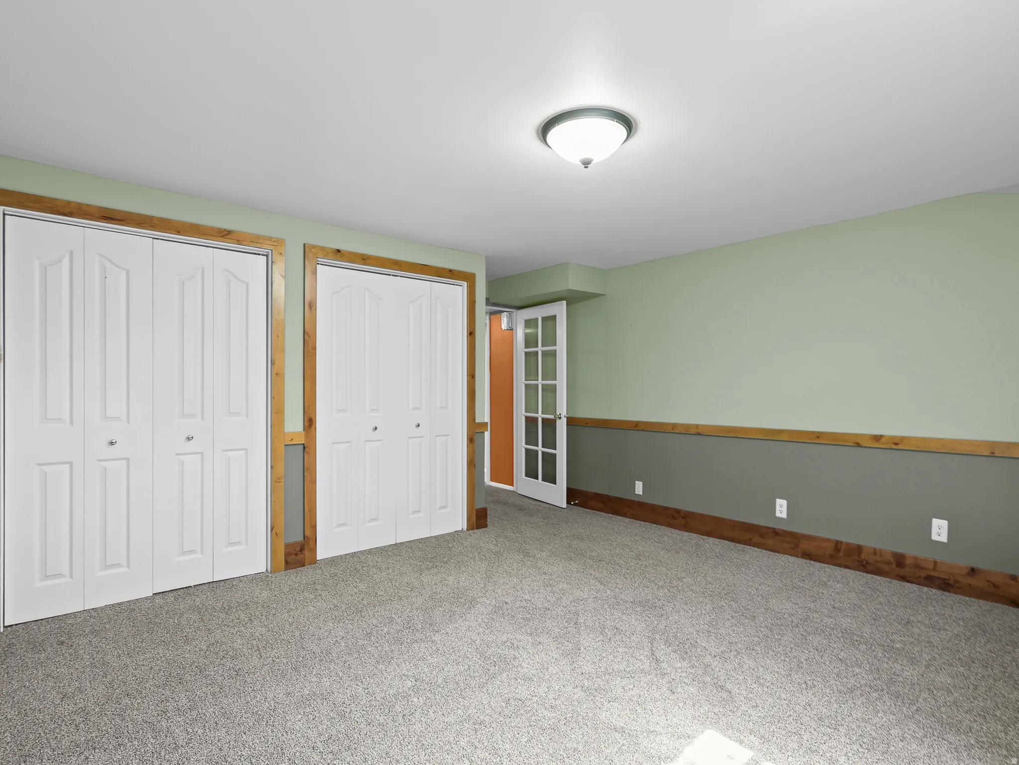 Spacious room featuring light gray carpeting, two-tone walls with a rustic wood-finish chair rail, and two sets of bi-fold closet doors