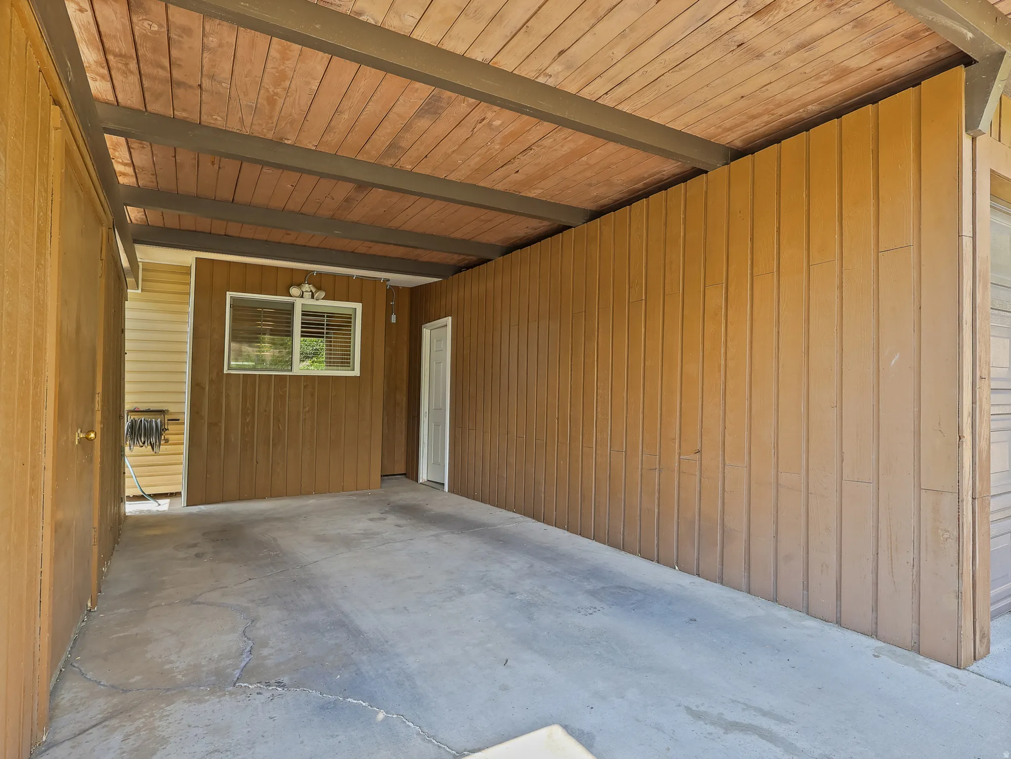 Carport featuring a wood-panel ceiling, concrete flooring, and vertical wood-plank siding