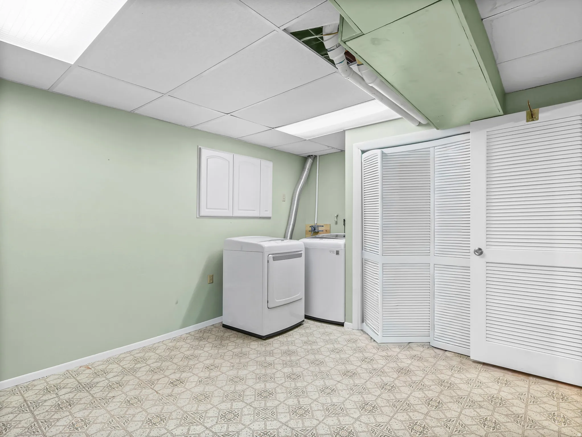 Utility room featuring a drop ceiling, patterned vinyl flooring, and wall-mounted cabinetry