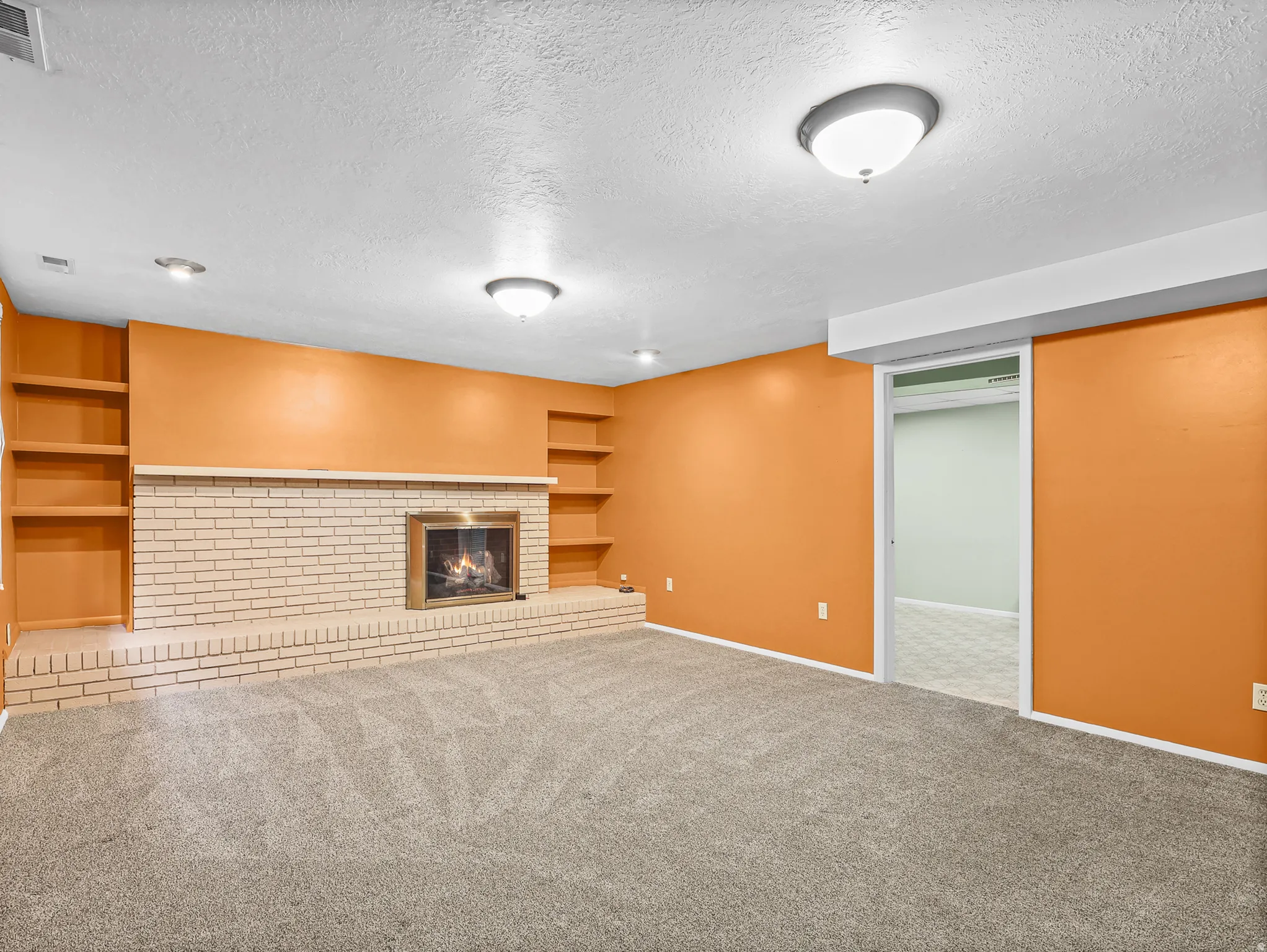 Spacious room featuring a brick fireplace with a raised hearth, built-in shelving, neutral carpet flooring, and recessed lighting