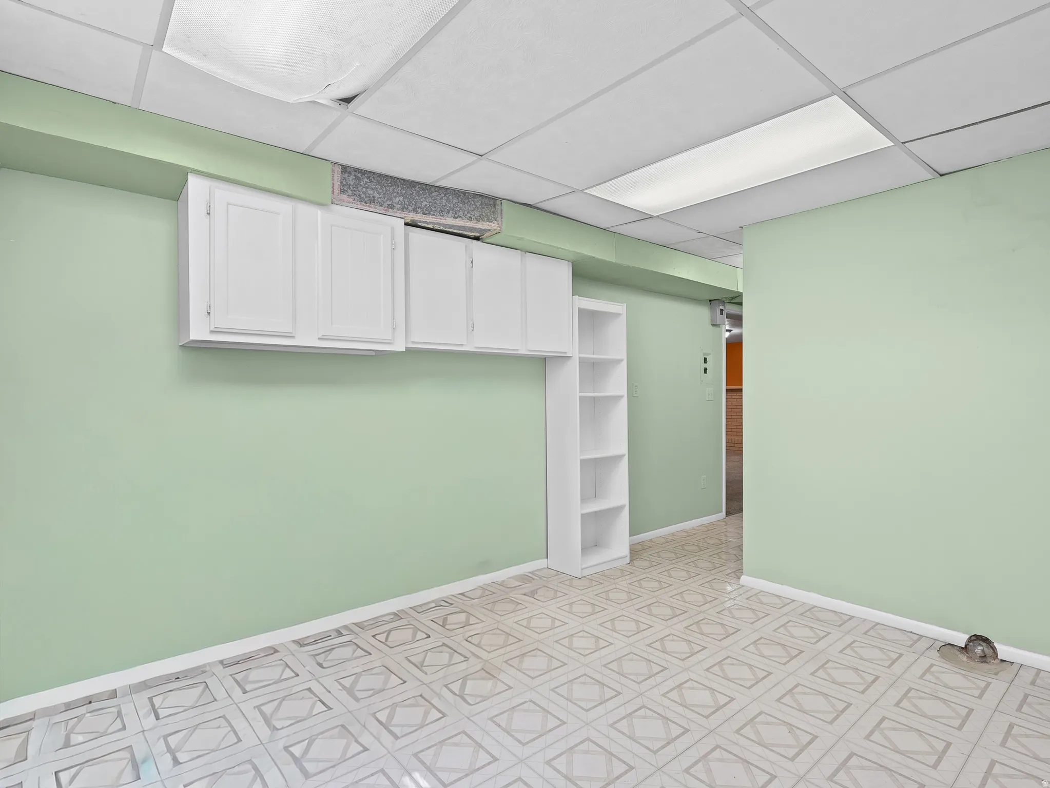 Spacious room featuring patterned floor tiling, built-in white cabinetry, open shelving, and a drop ceiling with recessed lighting