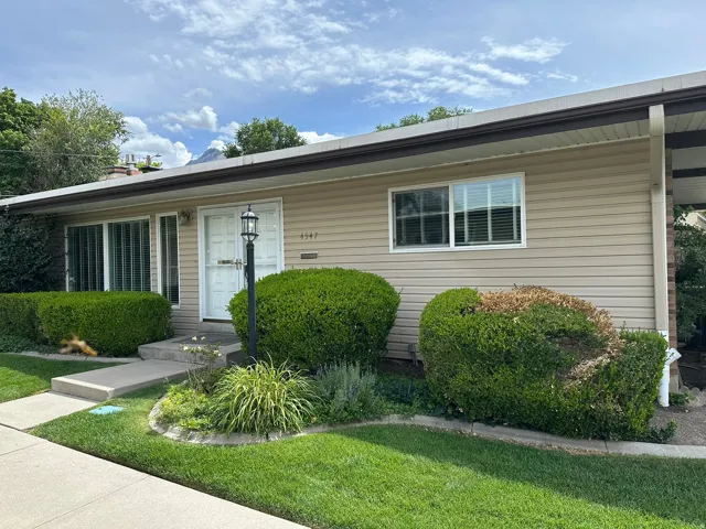 Cream-colored horizontal siding, white entry door with a screen door, front yard landscaping, concrete walkway, and a decorative light post