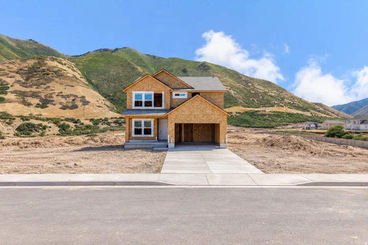 Newly constructed residence featuring a two-car garage, multiple windows, and a paved driveway, set against a mountainous backdrop