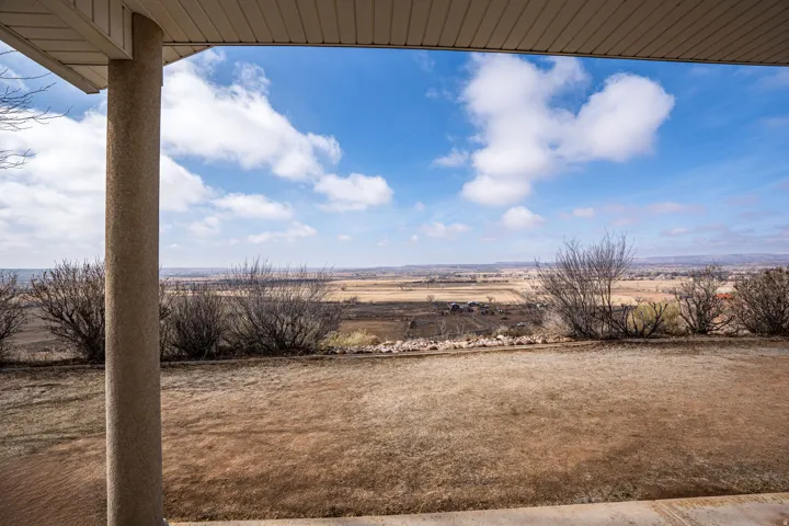 Expansive outdoor area featuring a wide panoramic landscape, mature shrubbery, a concrete patio, and an overhead soffit
